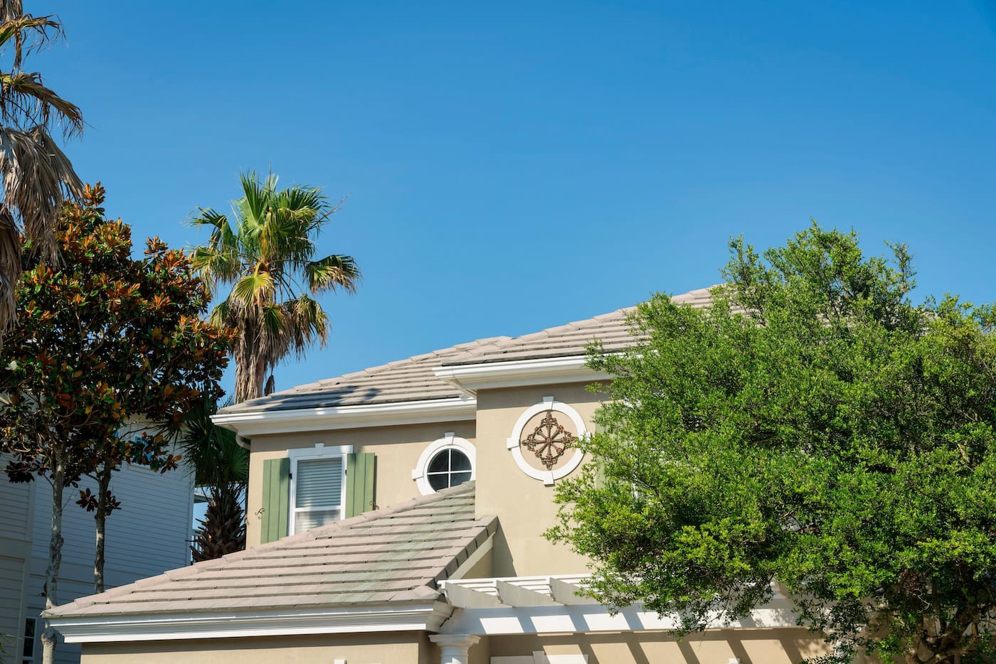 Top exterior of a house with asphalt composite roof shingles at Destin, Florida. There are trees outside the house with round trims with decorative panels and windows and a window with fake shutters.