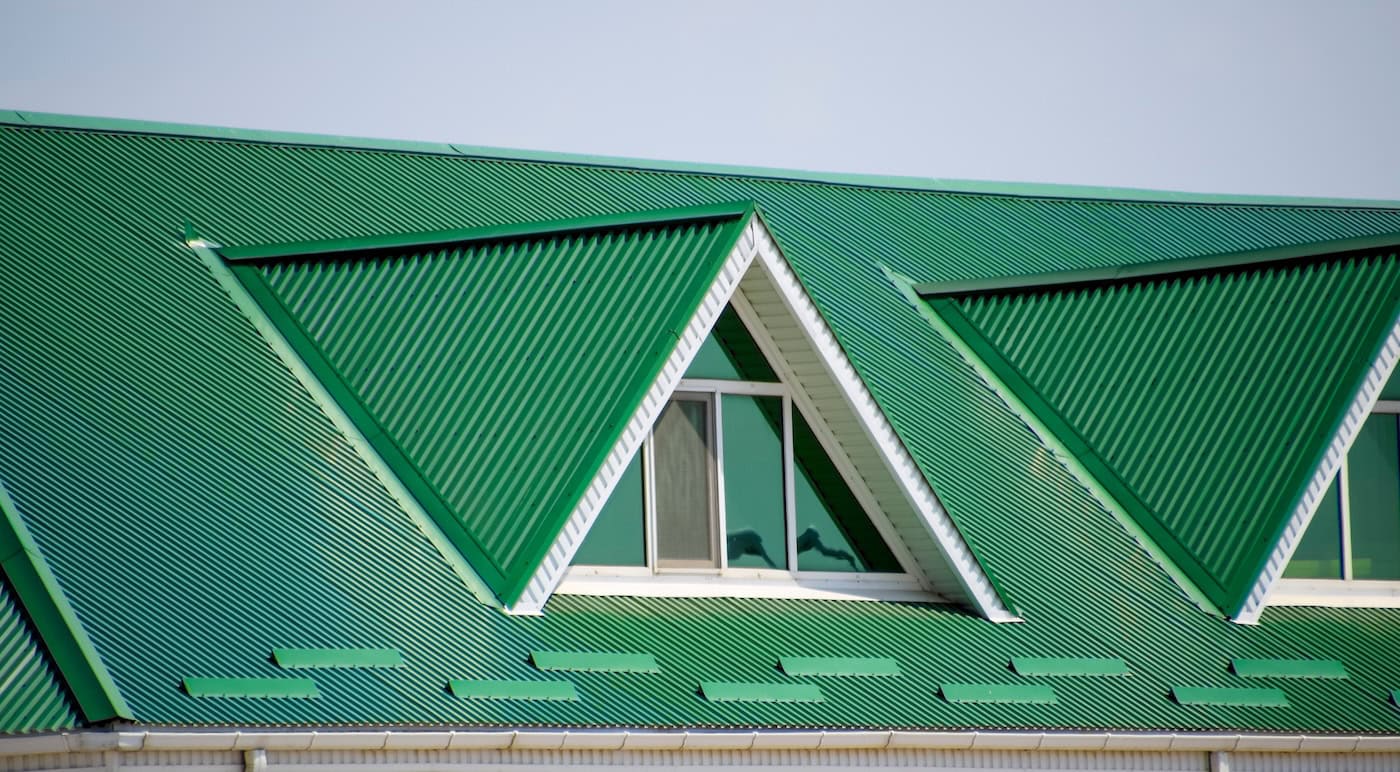 The house with plastic windows and a green roof of corrugated sheet. Roofing of metal profile wavy shape on the house with plastic windows. Green roof of corrugated metal profile and plastic windows.