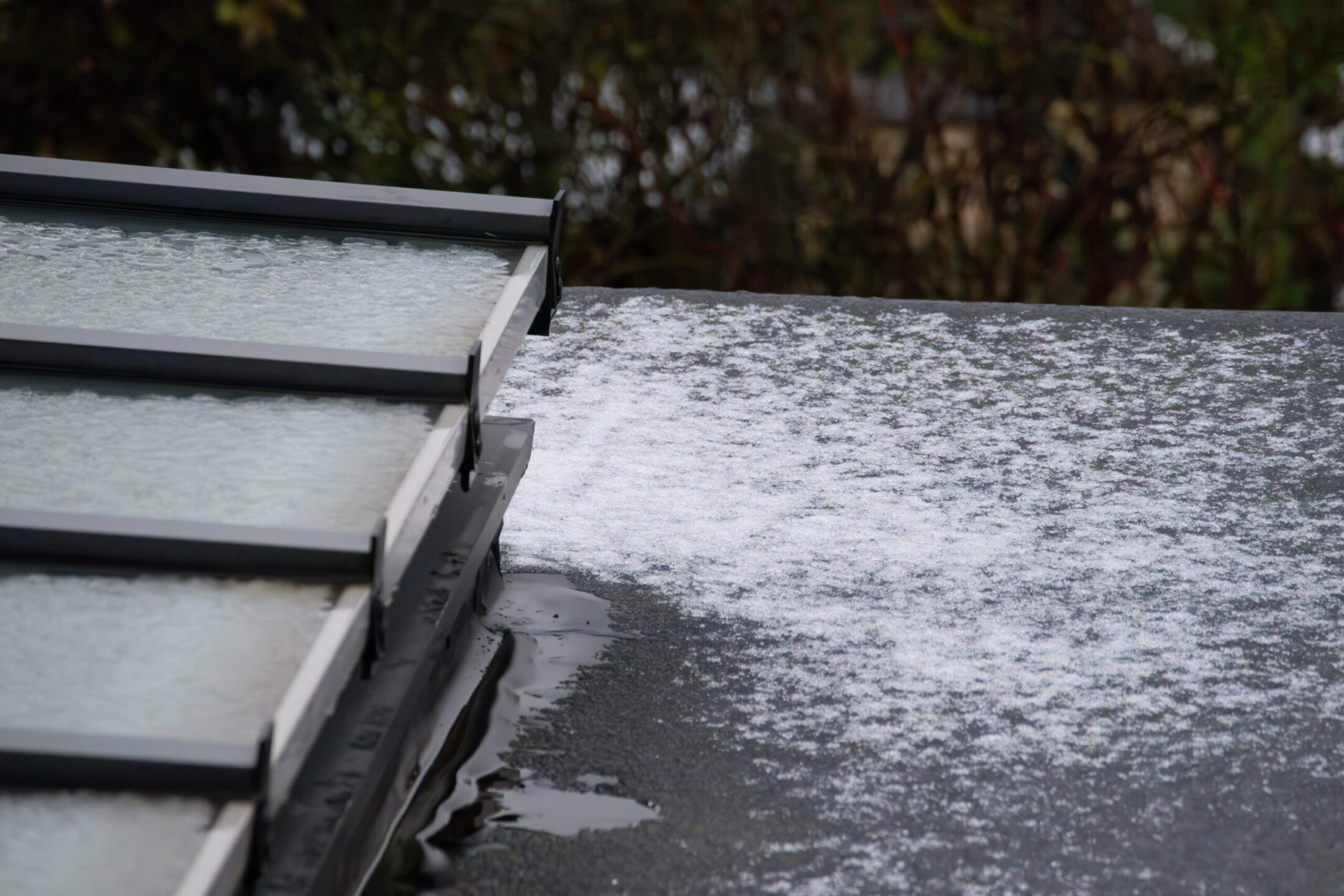 Close-up of flat roof and glass skylight covered in melting snow and ice in winter