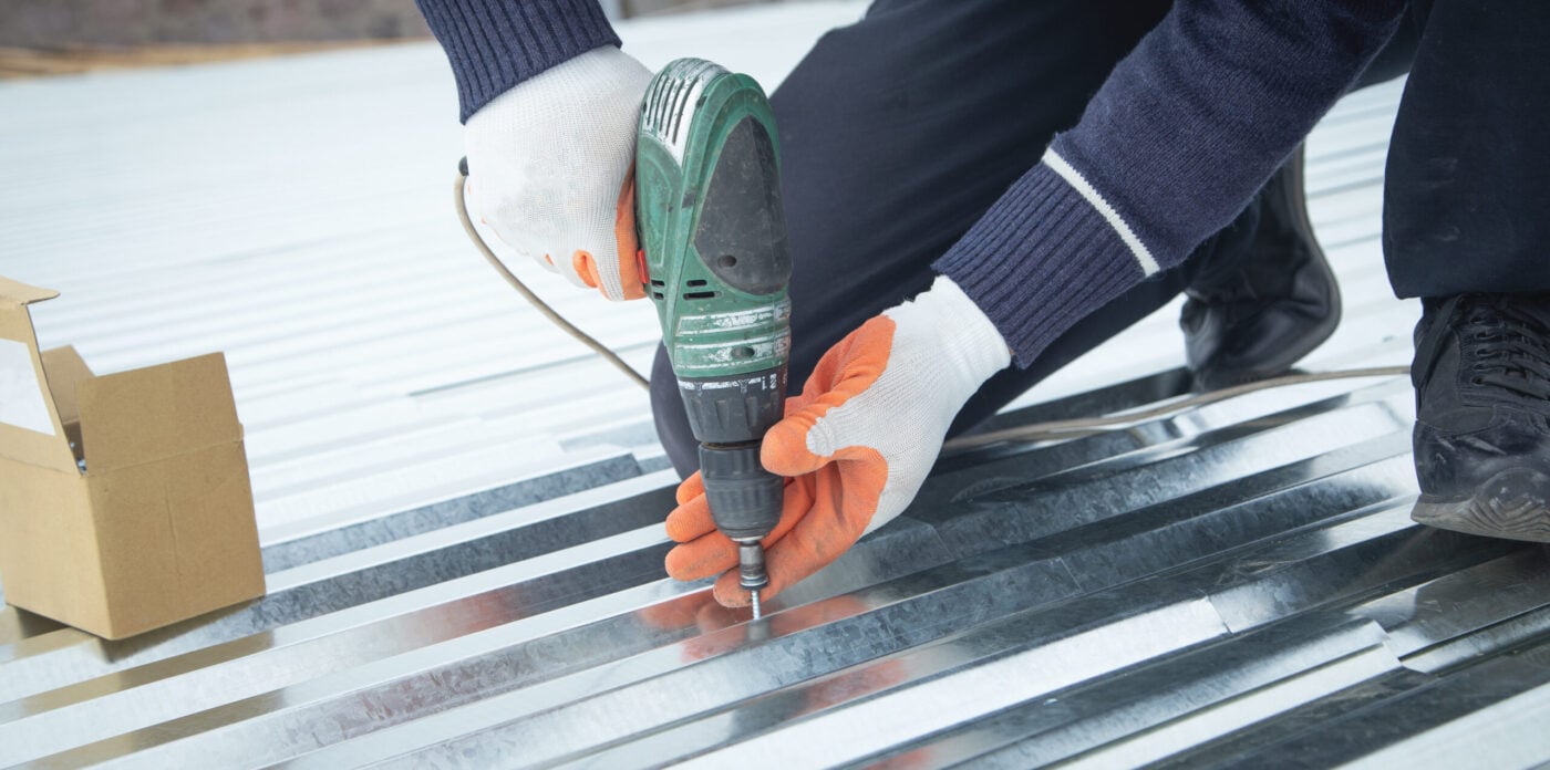 Man installing metal sheet roof by electrical drilling machine.