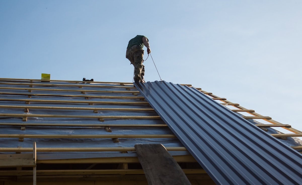 Worker pulls a metal roof panel into place on open rafters