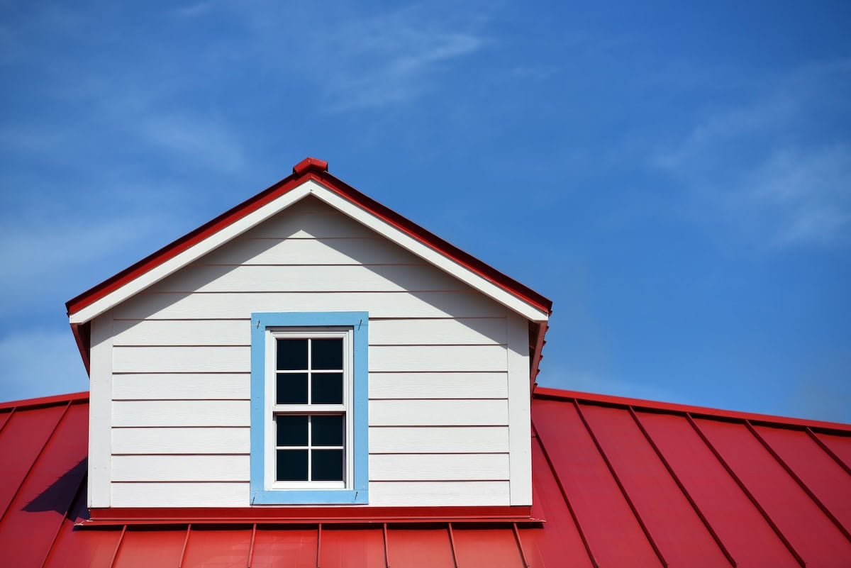 Red metal roof meets a white dormer with a blue-trimmed window