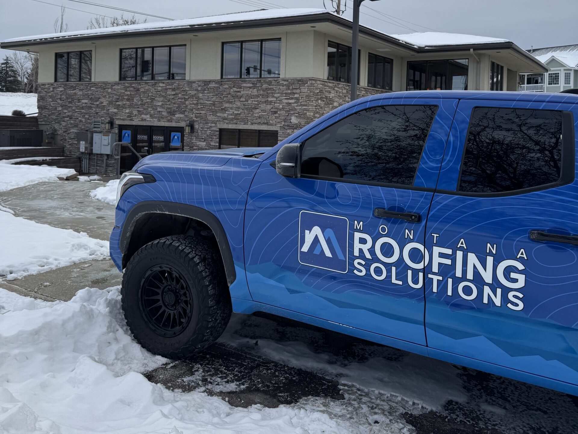 roof leak inspection branded blue truck outside house in winter